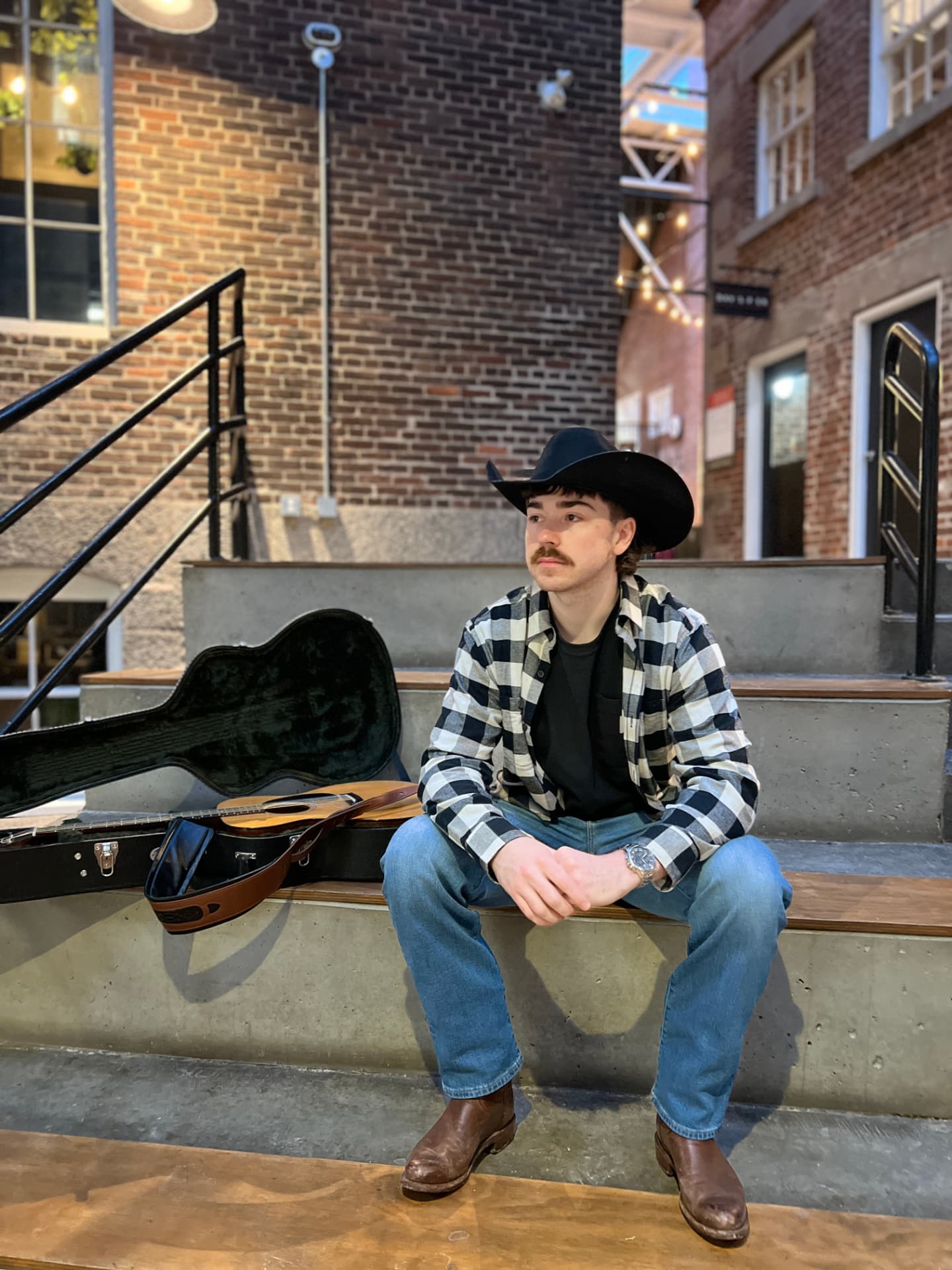 Josh Janes sitting on brick steps at night beside an open guitar case
