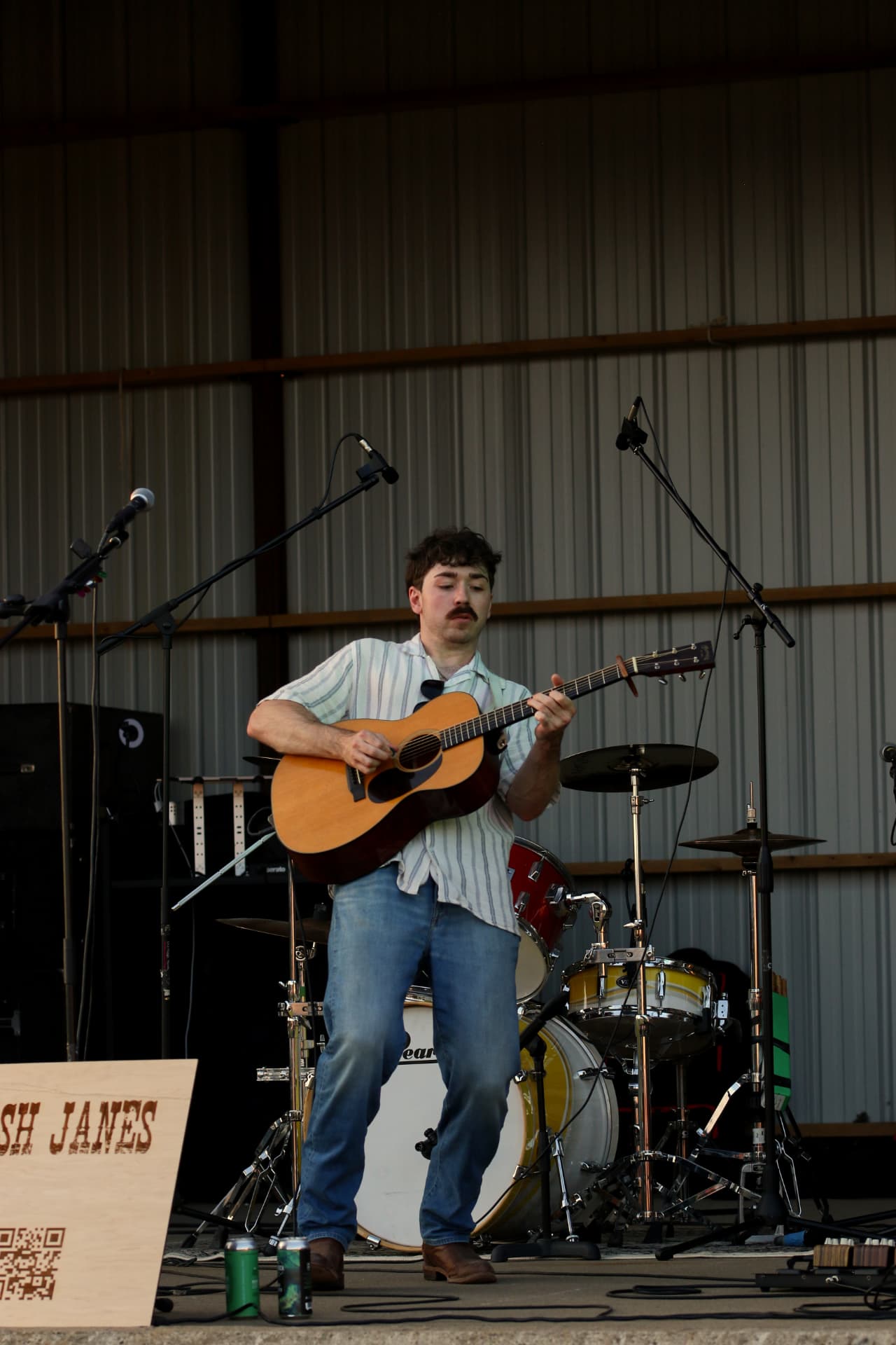 Josh Janes playing acoustic guitar in the evening light of an outdoor stage
