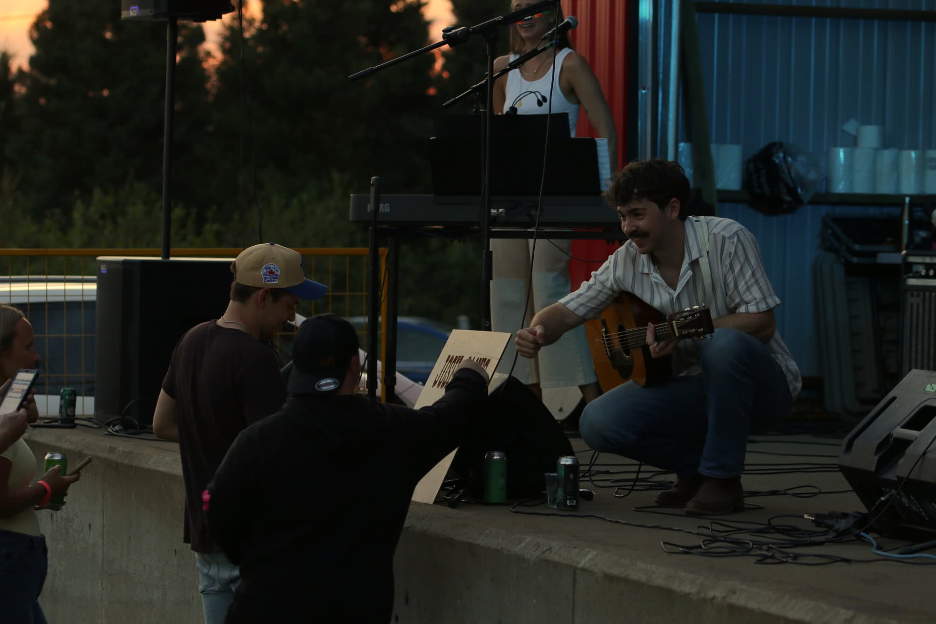Josh Janes crouching at the edge of the stage to talk with people at a show