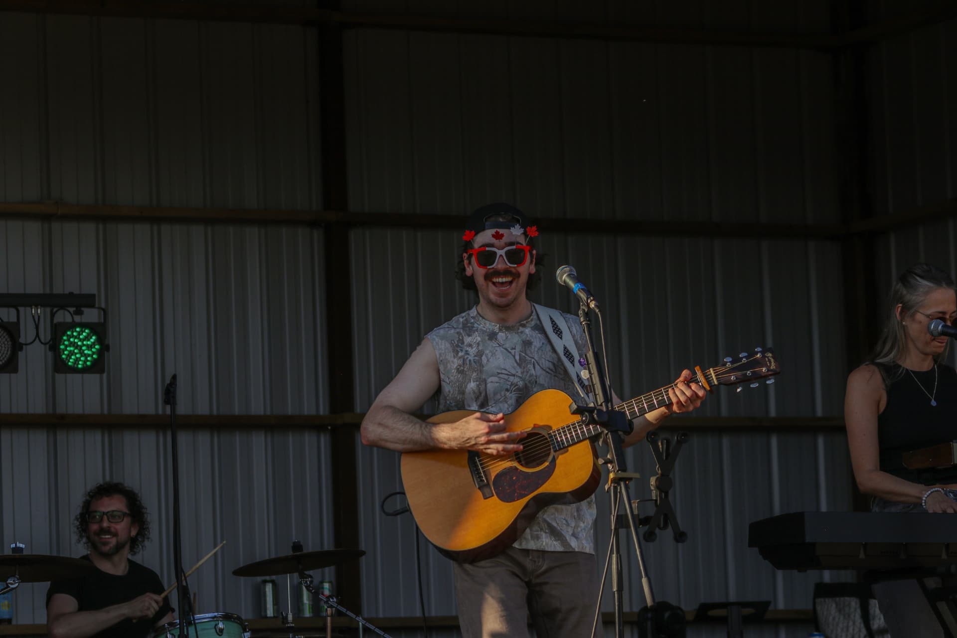 Josh Janes laughing on stage in Canada Day glasses with the band behind him